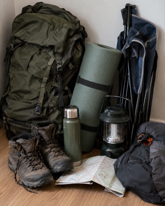 A packed backpack, hiking boots, a sleeping mat, and a lantern